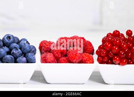 Fresh Raw Berries in white ceramic bowl on white background. Space for text. Red Currant, Raspberry and Blueberry, Summer Fruits Stock Photo