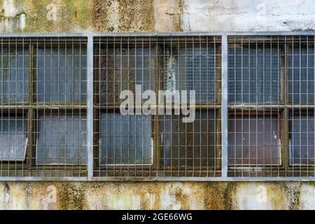 Factory windows covered in slime behind a security grill Stock Photo