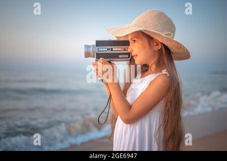 Girl with a retro vintage camera taking photos and film of a beautiful sea sunrise and beach