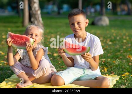 To cute kids lttle boy and girl eating juicy watermelon in the autumn park meadow. Stock Photo