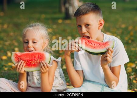 To cute kids lttle boy and girl eating juicy watermelon in the autumn park meadow. Stock Photo