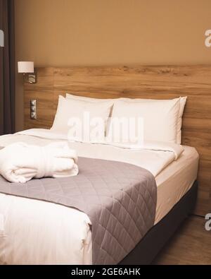 Modern hotel room with king-size bed made up with clean white pillows and sheets. Beige interior with wooden panels Stock Photo