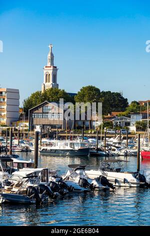 Arcachon (south western France): speedboats and sailboats in the marina with buildings and house along the waterfront, and steeple of the Church of Sa Stock Photo
