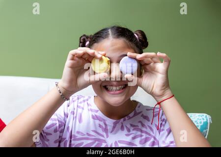 Latina teenager girl holding two macaroons in front of her eyes and smiling Stock Photo