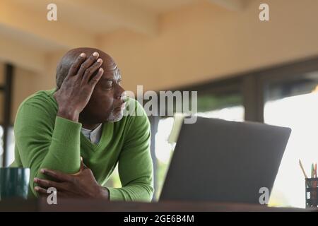 Thoughtful senior african american man in modern kitchen working on laptop Stock Photo