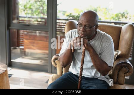 Thoughtful senior african american man sitting on armchair and leaning on the walking stick Stock Photo