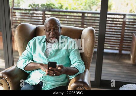 Senior african american man sitting on the armchair and using smartphone in the modern living room Stock Photo