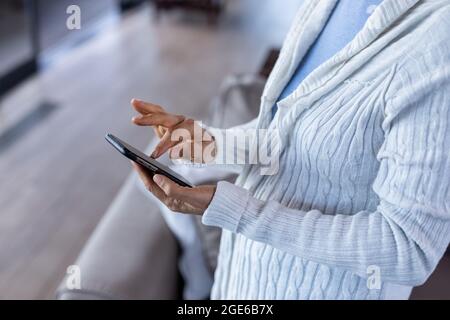 Midsection senior caucasian woman in living room standing and using mobile phone Stock Photo