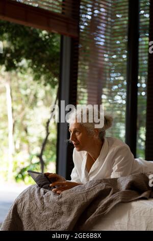 Senior caucasian woman lying on the bad and using tablet Stock Photo