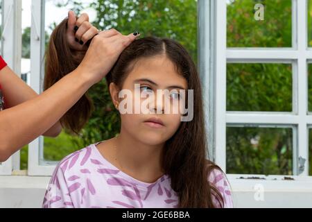 Latina girl sits pensively while having her hair combed near a window. Stock Photo