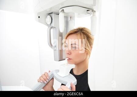 Young woman making panoramic shot of the jaw holding her face at the x-ray machine Stock Photo