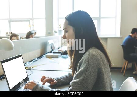 An adult girl uses a laptop with a blank white screen for mockup Stock Photo