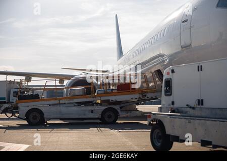 Baggage on conveyor belt unloaded from an airplane outdoors on a daytime Stock Photo