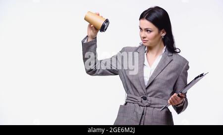 Businesswoman with clipboard looking at empty paper cup isolated on white Stock Photo