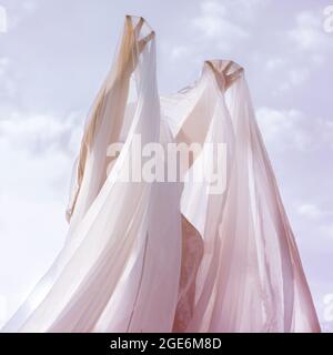 Woman covered with veil or thin cloth stands against the sky with her hands raised up Stock Photo