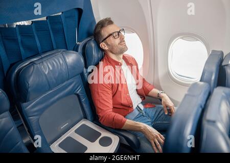 Handsome caucasian man in casual wear resting on the plane, sitting near the window Stock Photo