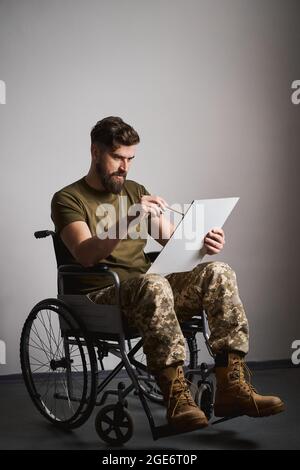 Young military man sitting in a wheelchair and painting on a canvas Stock Photo