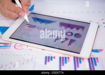Businessman planning about graph and chart of investment with report for finance on tablet computer on desk, statistic for financial and profit with d Stock Photo