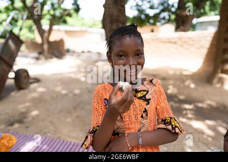 Stylish black African girl standing in her family's courtyard, grinning at camera while eating a boiled egg Stock Photo