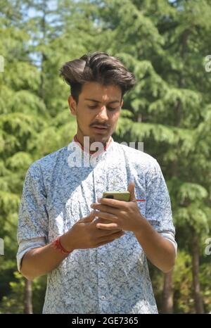 Portrait of a Indian handsome young guy standing outside with using mobile phone Stock Photo