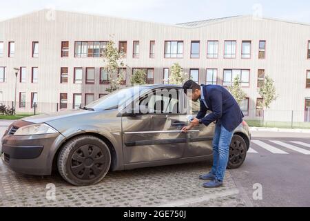 Profile of brunette man wearing jeans and jacket, car inspection for insurance claim the automobile, assesses the damage to the vehicle, examines care Stock Photo