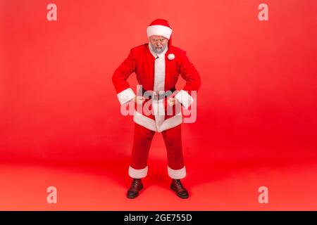 I am strong. Portrait of funny elderly man with gray beard wearing santa claus costume standing looking at camera with proud face, demonstrating power Stock Photo