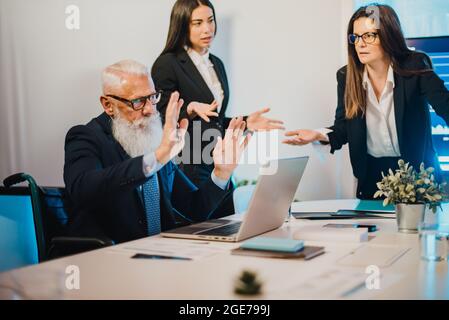 Business trader team discussing crypto market financial growth inside bank office - Focus on senior man on wheelchair Stock Photo