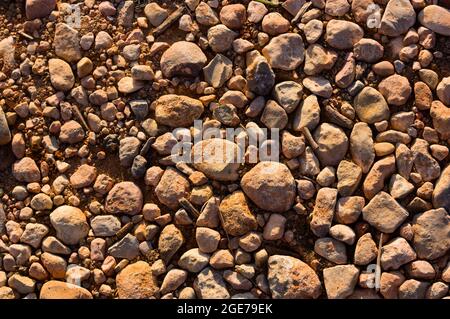 Close-up of a rural road formed by abundant small stones on compacted earth and illuminated by the setting sun that adds texture to the image Stock Photo