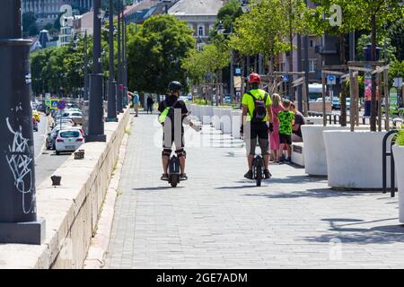 Two young men riding unicycle in street along Danube River, Budapest, Hungary Stock Photo