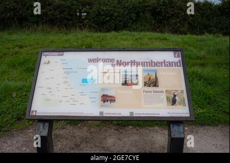 Welcome to Northumberland sign at English border with Scotland. Shows map and places of interest. All text readable. Blurred background of grass. Stock Photo