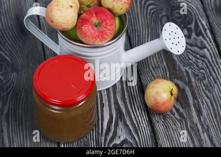 Green apples in a metal watering can.  On pine boards. Nearby is a jar of jam. Harvest apples. Stock Photo