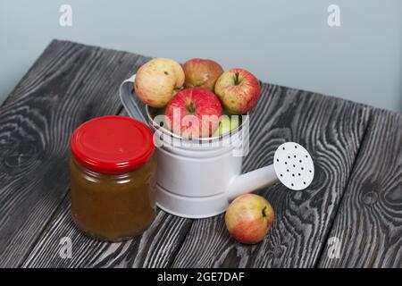 Green apples in a metal watering can.  On pine boards. Nearby is a jar of jam. Harvest apples. Stock Photo