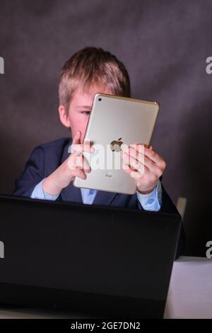 A happy boy in a school suit with a digital tablet in his hands, copy space on a dark studio background - Moscow, Russia, February 05, 2021 Stock Photo