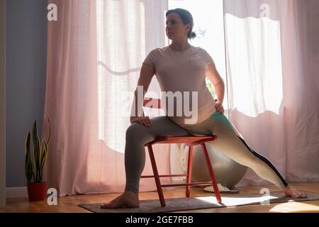Prenatal yoga at home. Full length pregnant woman doing yoga exercise stretching legs. Stock Photo