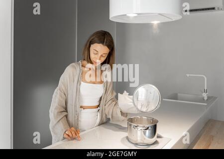 Young stylish woman cooking on induction hob at modern kitchen. Concept of smart technologies of kitchen appliances Stock Photo