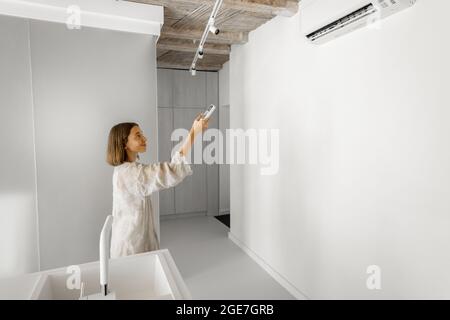 Woman sets the temperature on the air conditioner at home Stock Photo