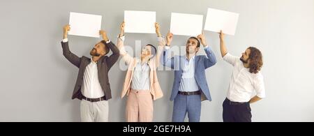 Group of happy business people standing in studio and holding white mockup banners Stock Photo