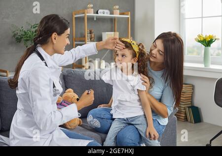 Female pediatrician checks the temperature of a little girl patient during a home visit. Stock Photo