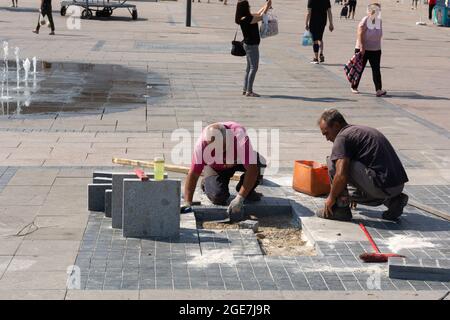 Nis, Serbia - August 14, 2021 Two repairmen repairing the sidewalks with tools in the town square in the city of Nis on a hot sunny summer day Stock Photo