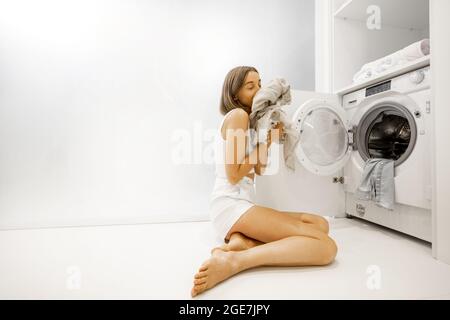 Young woman takes out freshly washed clothes from a washing machine in a bathroom at home Stock Photo