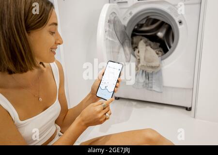Woman controls washing machine with a cell phone Stock Photo