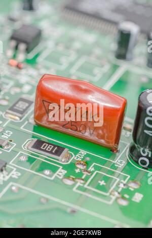 Close shot of orange coloured dipped polyester film capacitor on green pcb. For leaded capacitor, small electronic components. Maker unidentified Stock Photo