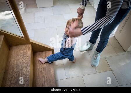 Toddler about to walk up wooden staircase assisted by mother, England. Stock Photo