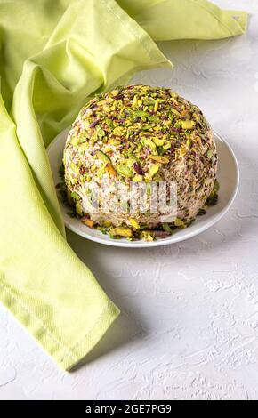 Sesame halva with pistachios on white plate on white background with green linen napkin. High angle view. Traditional middle eastern sweets. Jewish, t Stock Photo