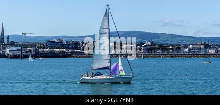 A yacht departing Dun Laoghaire Harbour in Dublin, Ireland. The town of Dun Laoghaire is in the background. Stock Photo