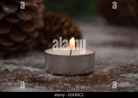 burning candle on a wooden table against the background of pine cones Stock Photo