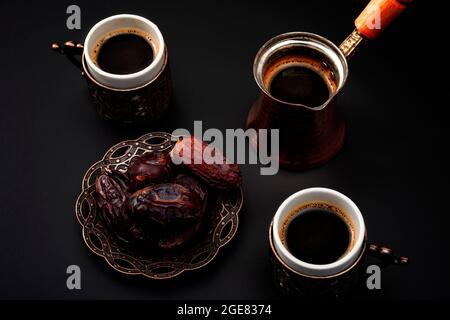 Middle eastern hospitality, dried fruit and traditional deserts concept theme with coffee pot, small cups and dates isolated on black background Stock Photo