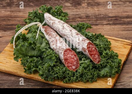 Spanish Fuet sausage with salad leaves over wooden background Stock Photo