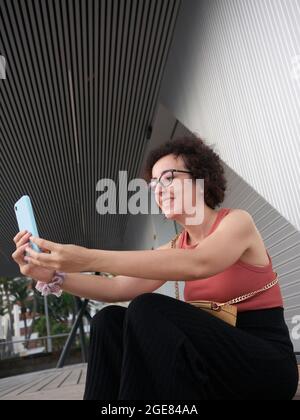 Woman taking a selfie in front of a modern city building Stock Photo
