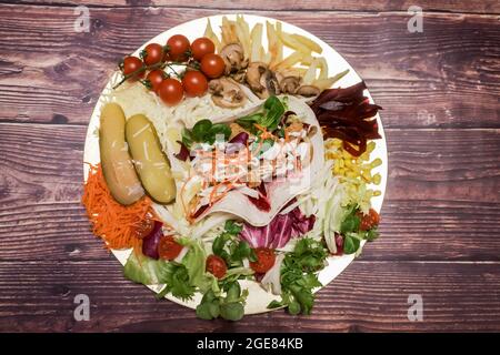 Plate of Chicken Fajitas with Vegetables, cherry tomatoes, pickles, corn, salad, carrots, beets, mushrooms, French fries and grated cheese, on a woode Stock Photo